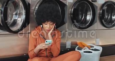 在洗衣店用智能手机微笑的年轻女人。 非裔美国学生在智能手机上有好消息。 自我